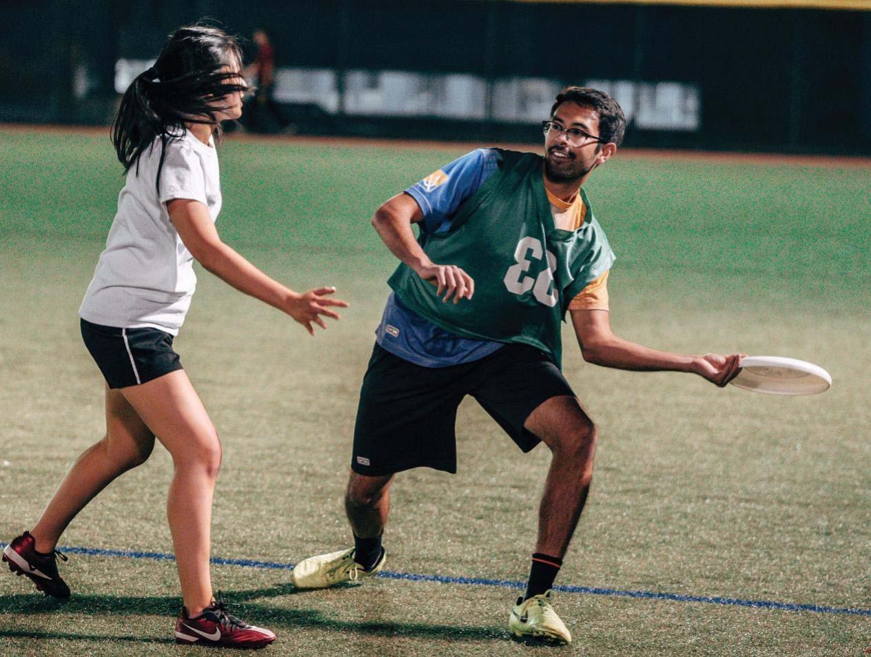 Two students playing frisbee outdoors at night on a lighted field.